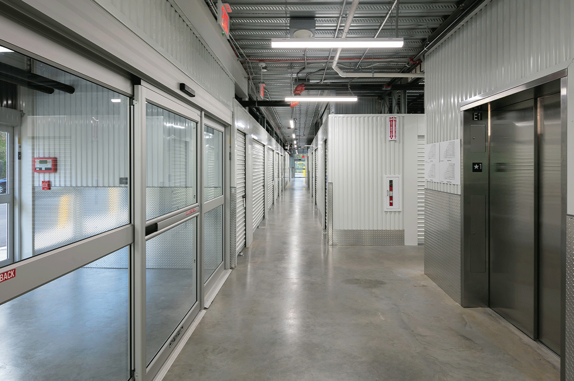 Image{width=1137,height=755,url='https://8488932.fs1.hubspotusercontent-na1.net/hubfs/8488932/HuntingtonGallery-4.png',altText='This is an interior shot showing the large, glass automatic doors across from the freight elevators. The hallways are brightly lit and each unit is secured with white roll-down doors. ',fileId=null}